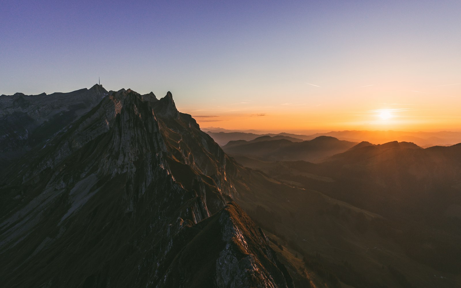 A climber on a snowy summit ridge at sunrise